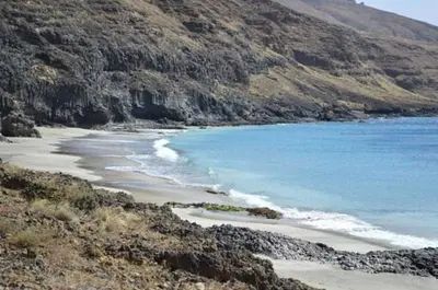 a beach with rocks and blue water and a mountain at TARRAFAL SN TOUR in Tarrafal