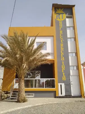 a building with a palm tree in front of it at Residencial Ribeira Torta in Porto Novo