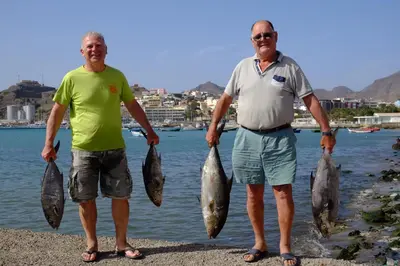 two men standing on the shore holding fish in their hands at Casa Comba in Mindelo