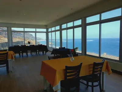 a dining room with tables and chairs and the ocean at Hotel Salinas São Jorge in São Filipe