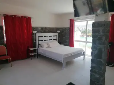 a bedroom with a bed with red curtains and a window at STUDIO VUE MER - CASA da LUZ in Mindelo