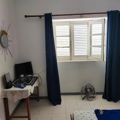 a room with a window with blue curtains and a desk at Casa fréd in Mindelo