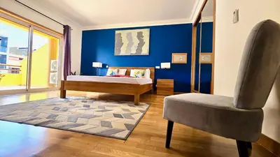 a bedroom with a bed and a chair and a blue wall at Spacious Penthouse with BBQ and Views in Praia
