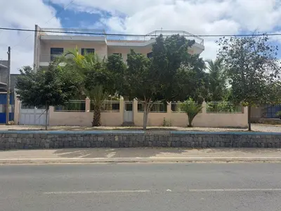 a white building with trees in front of a street at Barros Homestay in Tarrafal