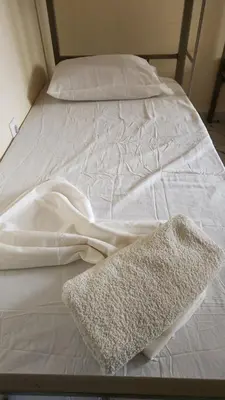 a white bed with a blanket and a rug on it at Please Read Email-Free EARLY Check In & Out-No Walk-Ins or Cash Accepted-Meeting Point Hostels in São Filipe