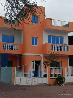 an orange house with a white fence in front of it at Magei in Tarrafal
