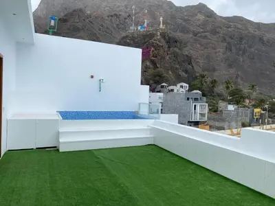 a white house with a green floor and mountains in the background at Laranjinha Rooms in Paul