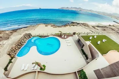 a building with a swimming pool next to the ocean at Apartamento T1 - Hotel Las Rochas in Mindelo