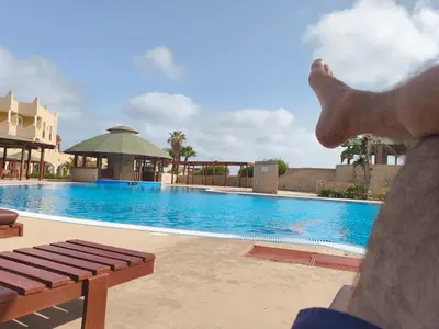 a person sitting on a bench next to a swimming pool at Marialva Tropical T2 in Santa Maria