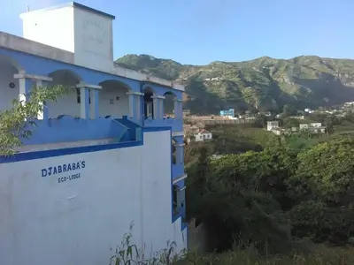 a blue and white building with mountains in the background at Djabraba's Trail Triple SUITE in Vila Nova Sintra