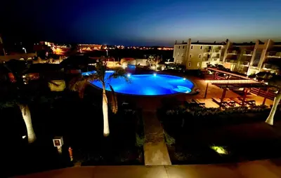 a swimming pool with palm trees and buildings at night at Tropical Oceano in Santa Maria