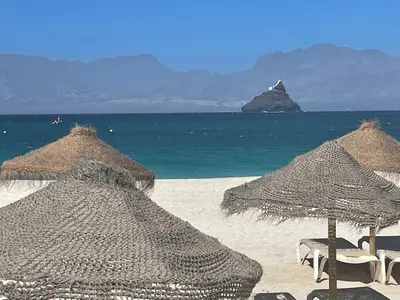 a group of straw umbrellas and chairs on a beach at Mindelo Bay Apartment in Mindelo