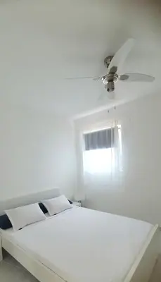 a white bed with a ceiling fan and a window at Residência Alto Saco, Ocean-view double room in Tarrafal