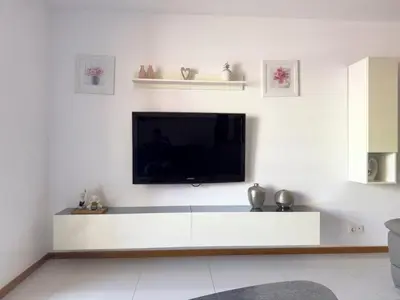 a living room with a tv on a white wall at Spacious 3-bdr apt seafront, exterior pool - LCGR in Praia