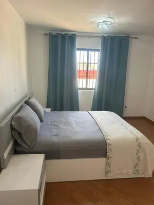 a bedroom with a bed with blue curtains and a window at Morabeza Lodge in Mindelo