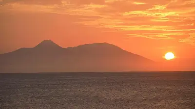 a sunset over the ocean with mountains in the background at Prainha Beach Home in Praia