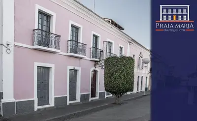 a pink building with balconies and a tree on a street at Pousada Praia Maria in Praia