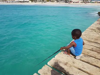 a young boy sitting on a dock holding a fishing pole at Sal Apartments Djadsal Moradias in Santa Maria