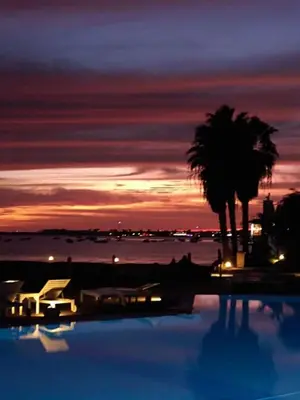 a swimming pool with a palm tree and a sunset at Porto Antigo - Charming & peaceful apartment overlooking pool and sea in Santa Maria