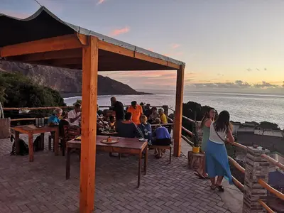 a group of people sitting at tables on a patio with the ocean at Kaza Ladera in Seladinha
