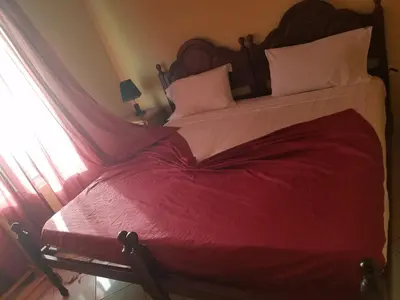 a large bed with a red comforter and a window at chez albino guest house in São Filipe