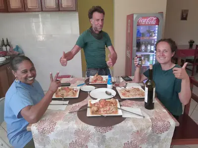 a group of people sitting around a table with pizza at chez albino guest house in São Filipe