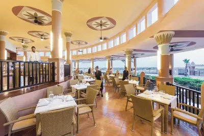 a restaurant with tables and chairs with the ocean in the background at Hotel Riu Funana - All Inclusive in Santa Maria