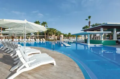 a swimming pool with white lounge chairs and umbrellas at Hotel Riu Cabo Verde - Adults Only - All Inclusive in Santa Maria