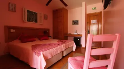 a bedroom with a bed and two pink chairs at Kira's Boutique Hotel in Mindelo