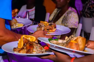a group of people holding plates of food on a table at Falucho Paradise Beach in Pedra Badejo