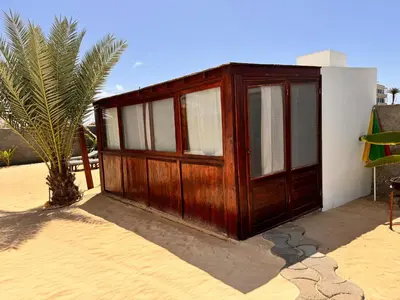 a wooden building sitting next to a palm tree at Vilas na areia aparthotel in Sal Rei