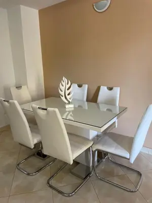 a dining room with a glass table and white chairs at Apartamentos Avenida in Praia