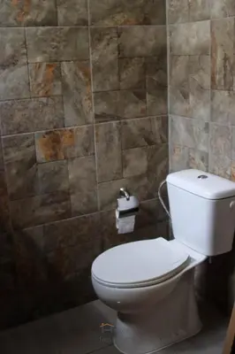 a bathroom with a toilet and a stone wall at Helton´s Residence in Praia